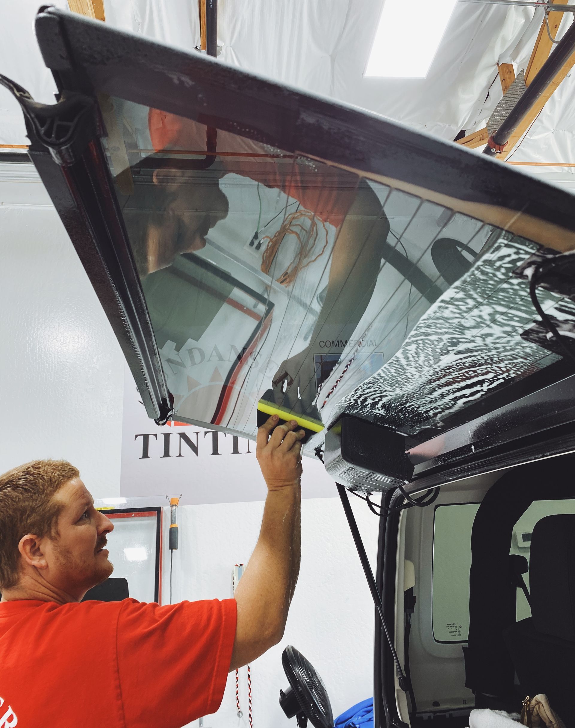 a man in a red shirt is applying tint to a car window