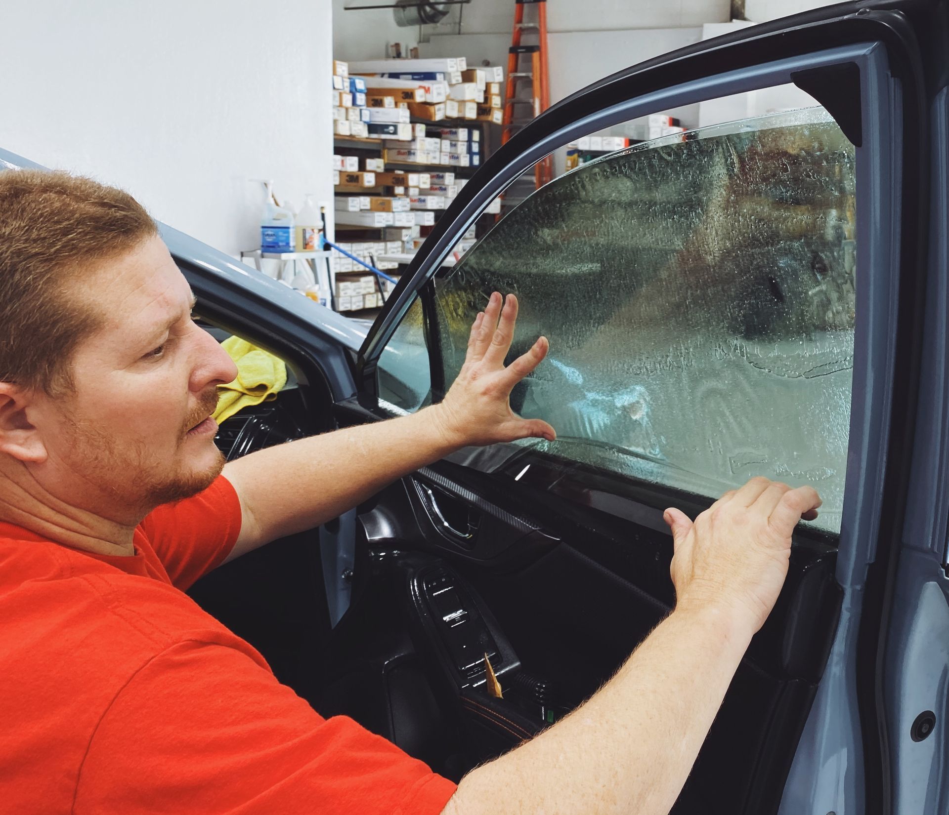 a man in a red shirt is working on a car window