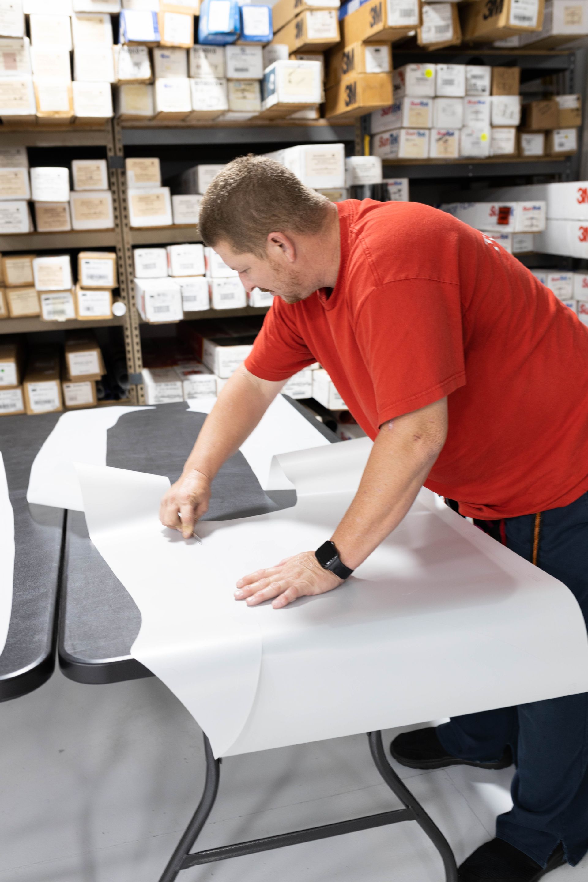 a man in a red shirt is cutting a piece of protective film on a table