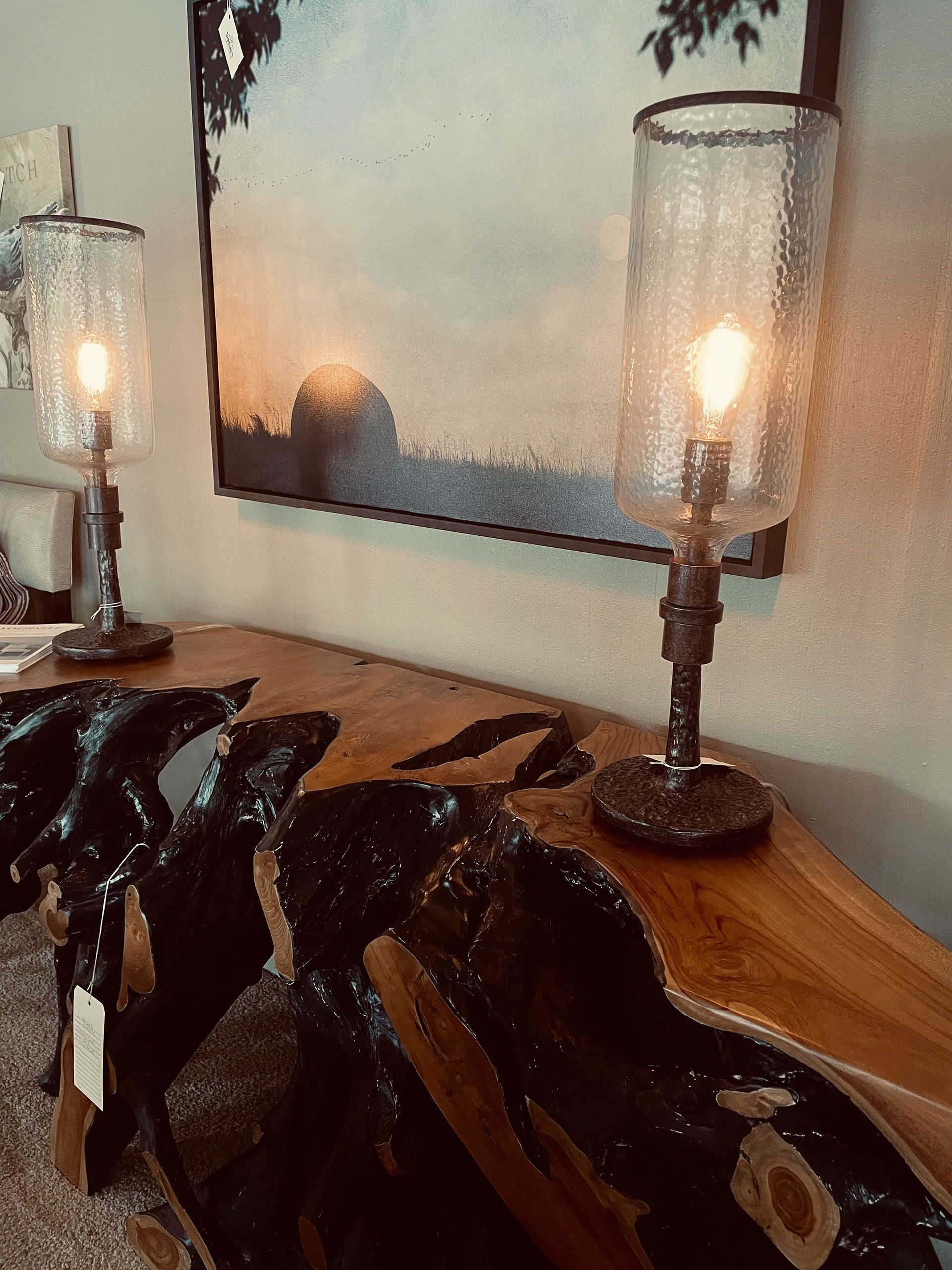 Two lamps are sitting on a wooden table in front of a painting.