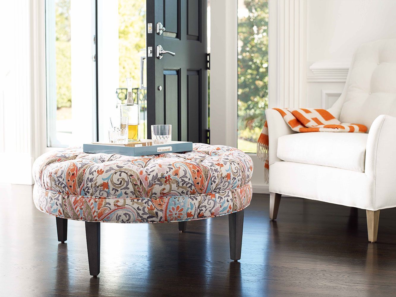 A living room with a floral ottoman and a white chair.