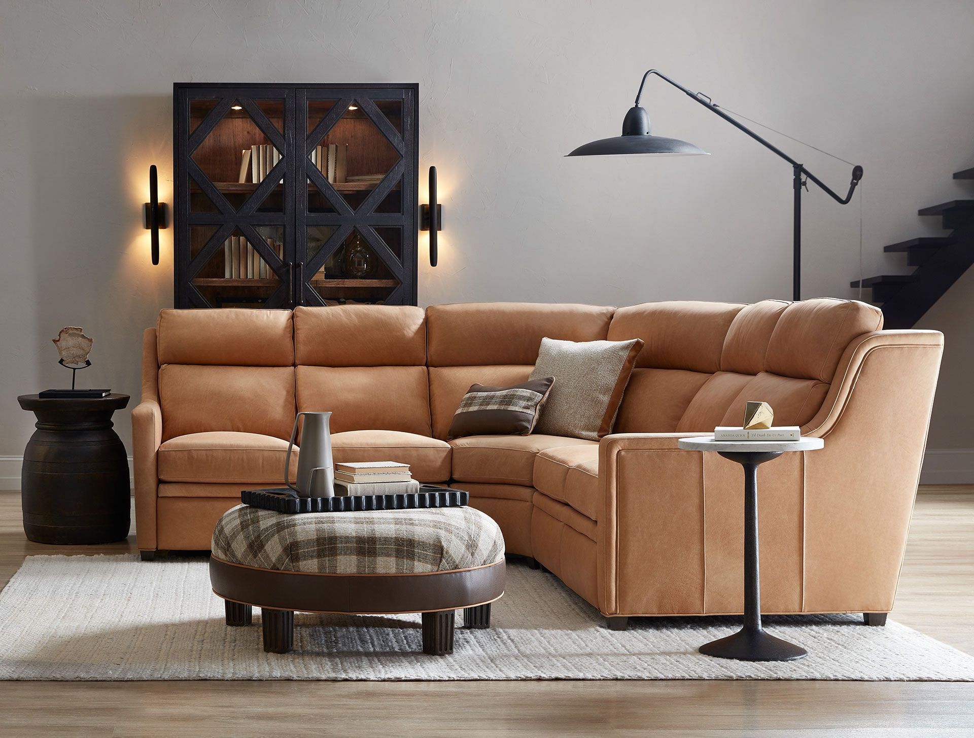 A living room with a sectional couch , ottoman , coffee table and lamp.