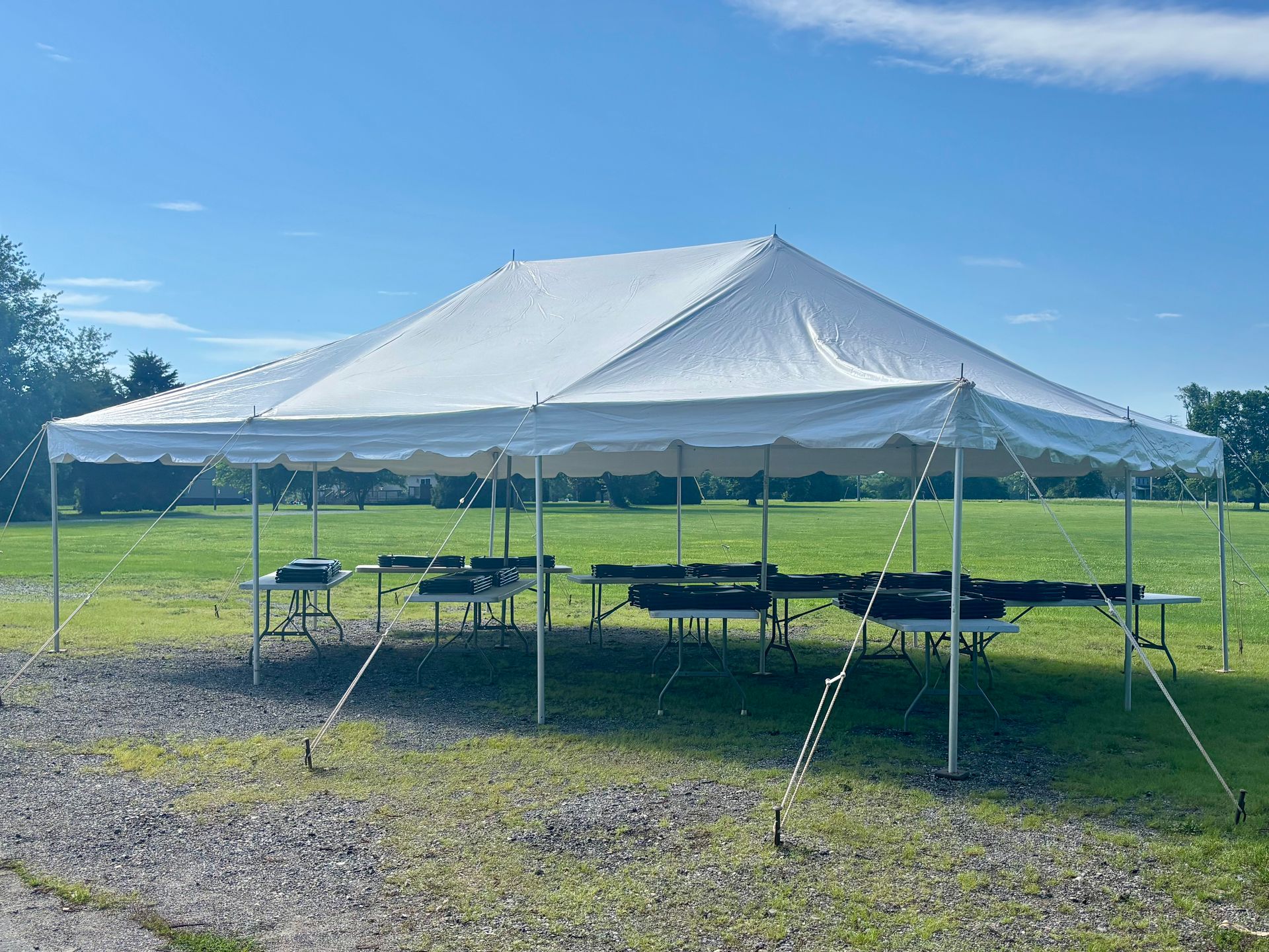 White event tent set up outdoors over tables. Green grass, blue sky.