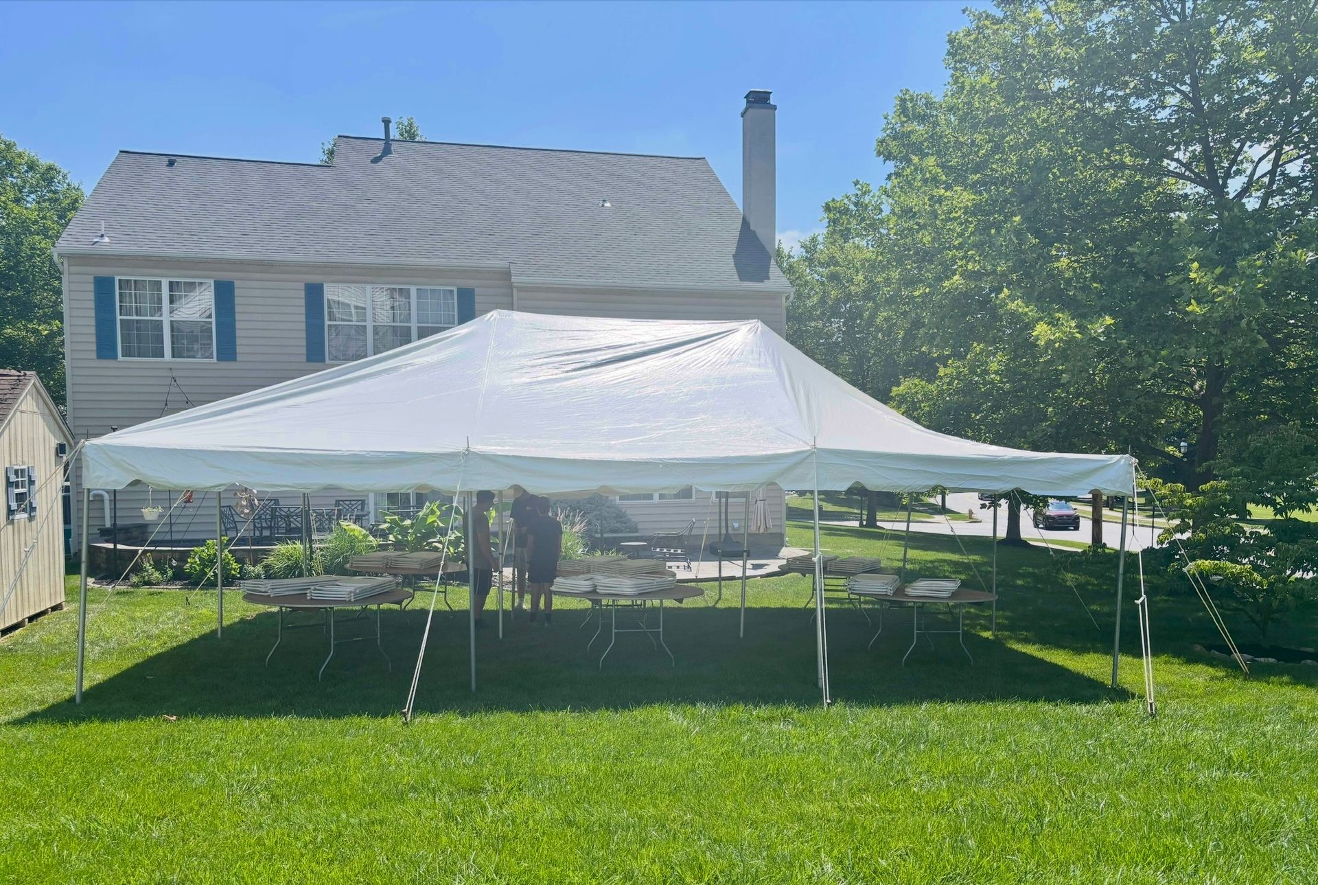 White tent set up in a backyard, with a house and trees in the background on a sunny day.
