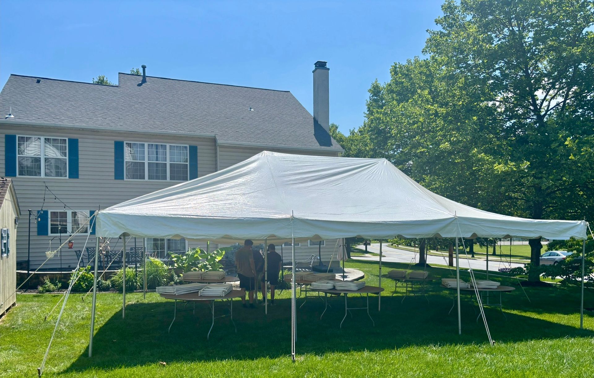 White tent set up in a backyard with tables underneath.  A two-story house is in the background.