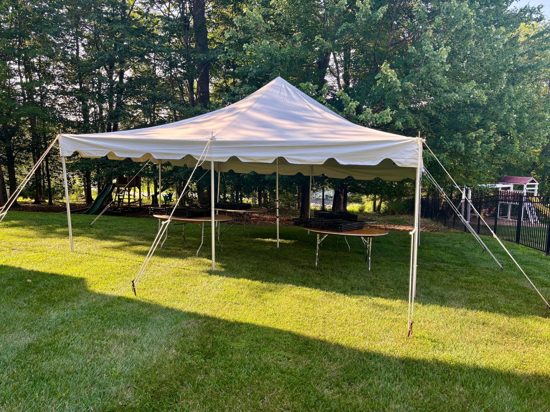 White tent set up on green grass with trees in the background, tables beneath the tent.