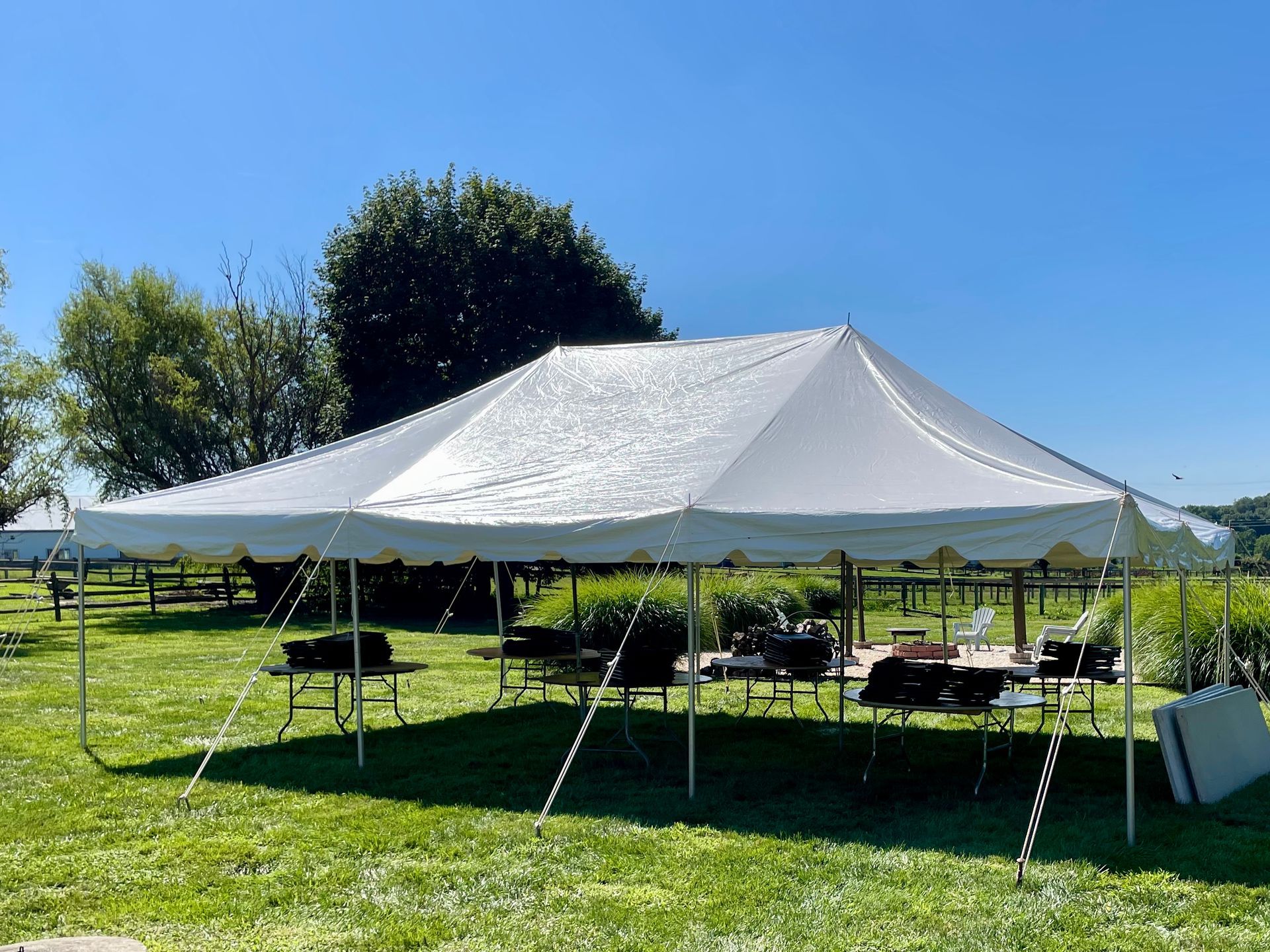 White tent set up on green grass, tables and chairs underneath, with blue sky.
