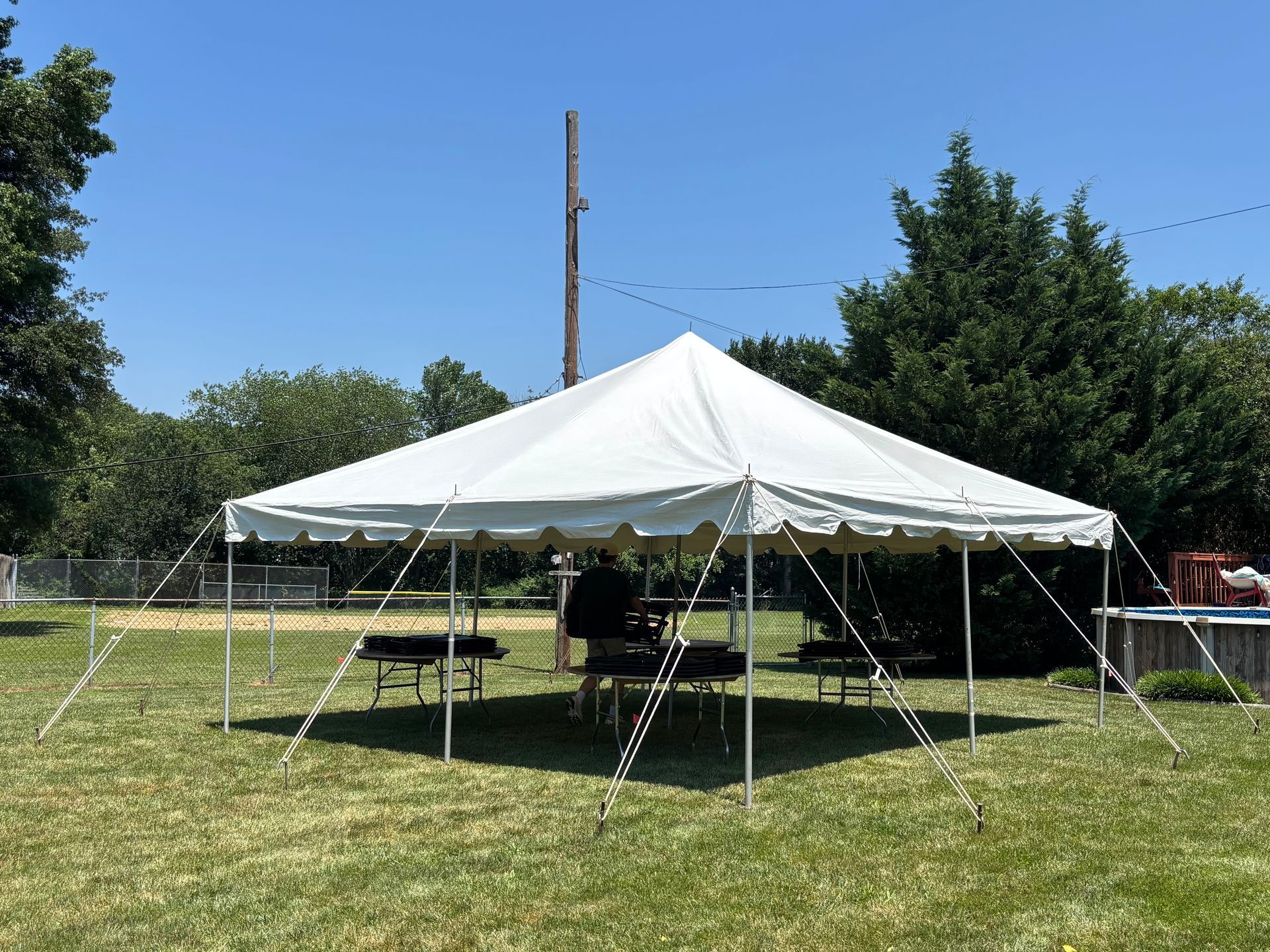 White tent set up in a grassy yard on a sunny day. Tables and chairs are inside the tent.