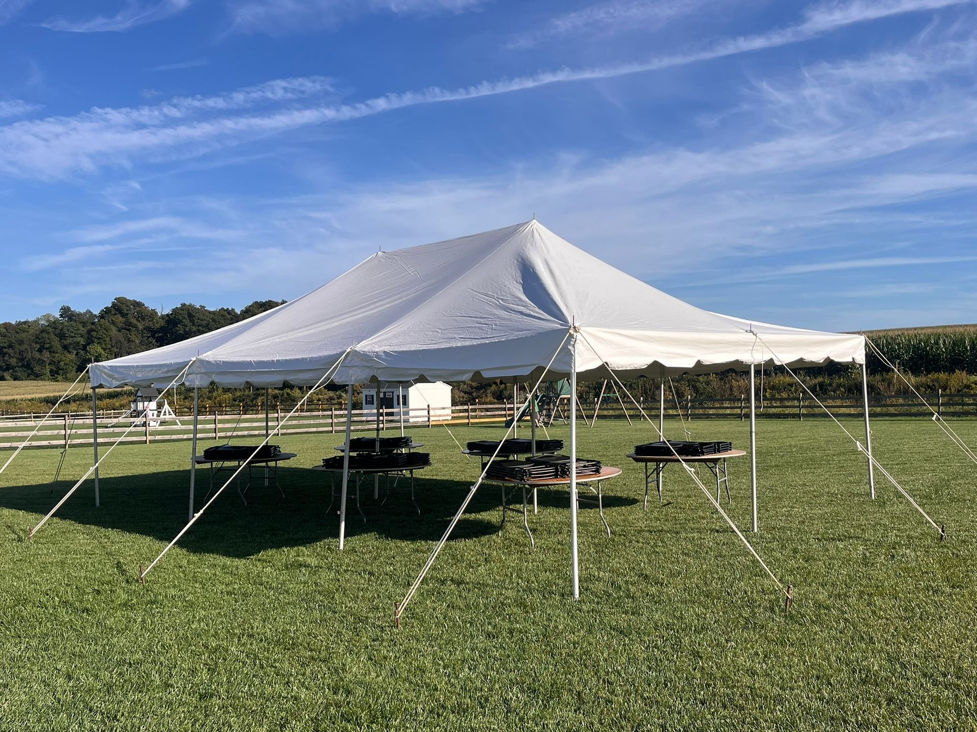 White tent set up on grassy field, with picnic tables underneath, sunny day.