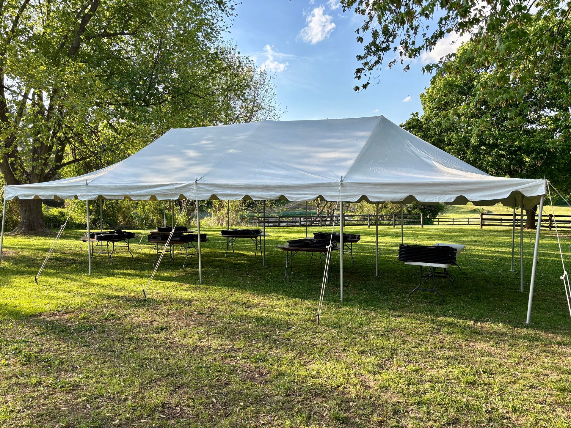 White tent set up outdoors, tables underneath, green grass and trees in background.