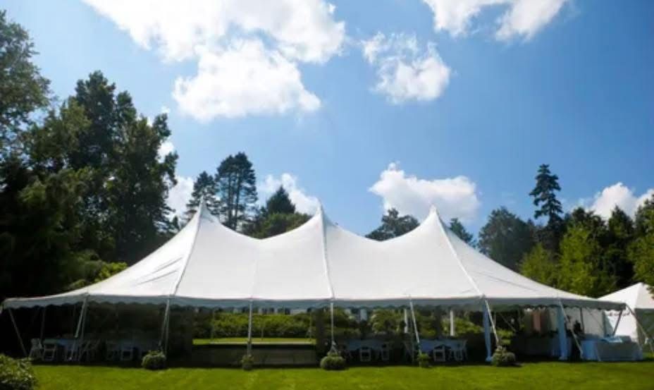 White tent set up on green grass under a blue sky with fluffy clouds.