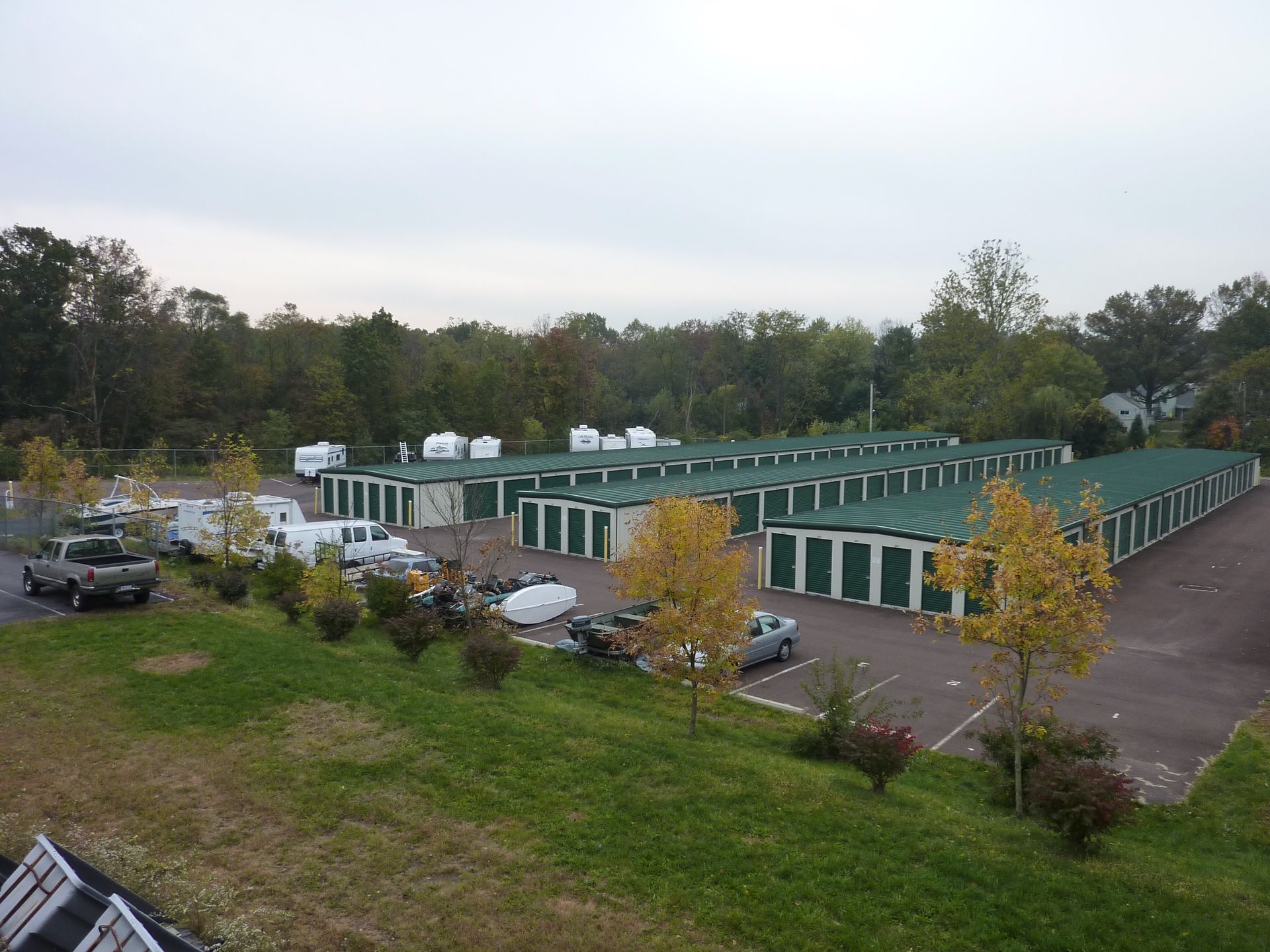 A row of green storage units are lined up in a parking lot.