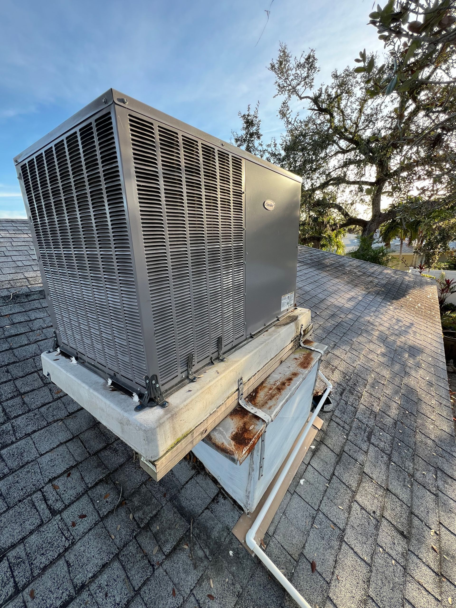 An air conditioning unit on a weathered rooftop with a partly cloudy sky in the background.