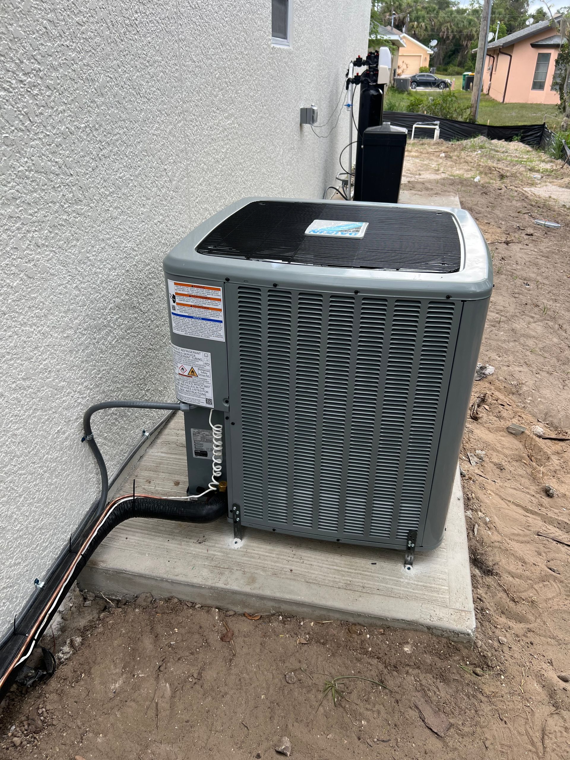 An air conditioning unit is installed on a concrete slab next to a stucco wall, outdoors.