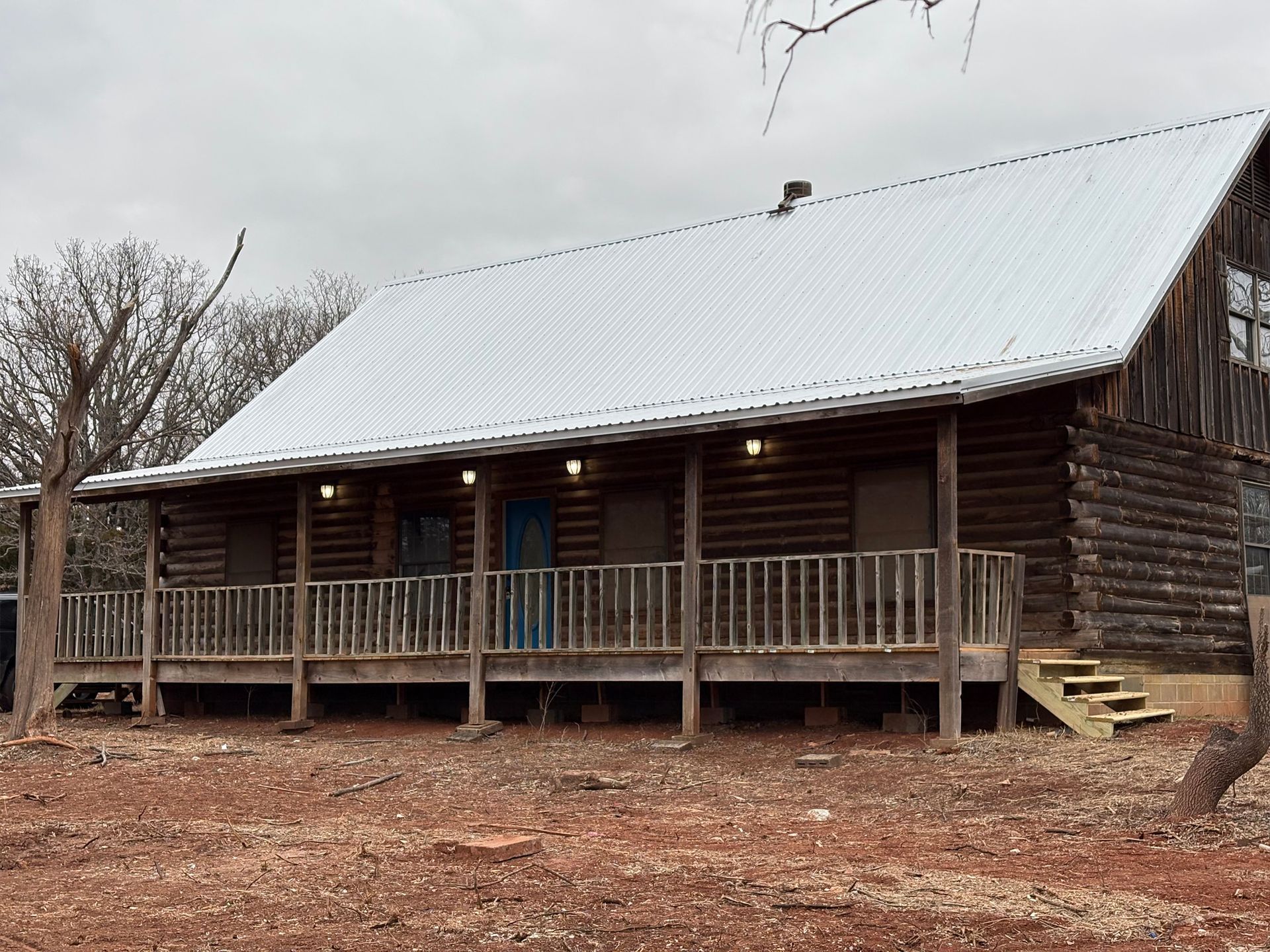 A log cabin with a porch and a metal roof is covered in snow.