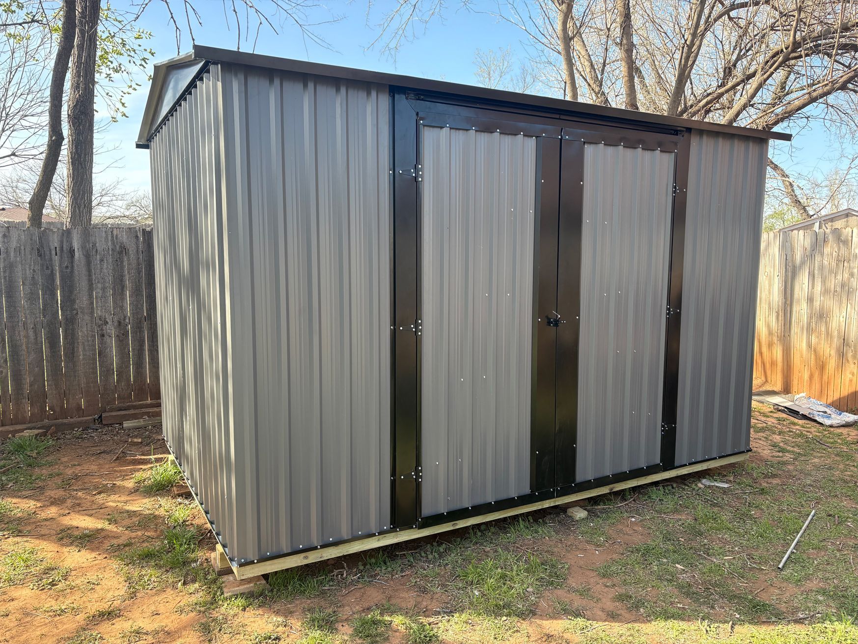 A gray metal shed is sitting in the grass next to a wooden fence.