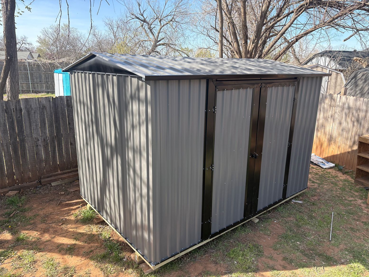 A gray metal shed is sitting in a backyard next to a wooden fence.