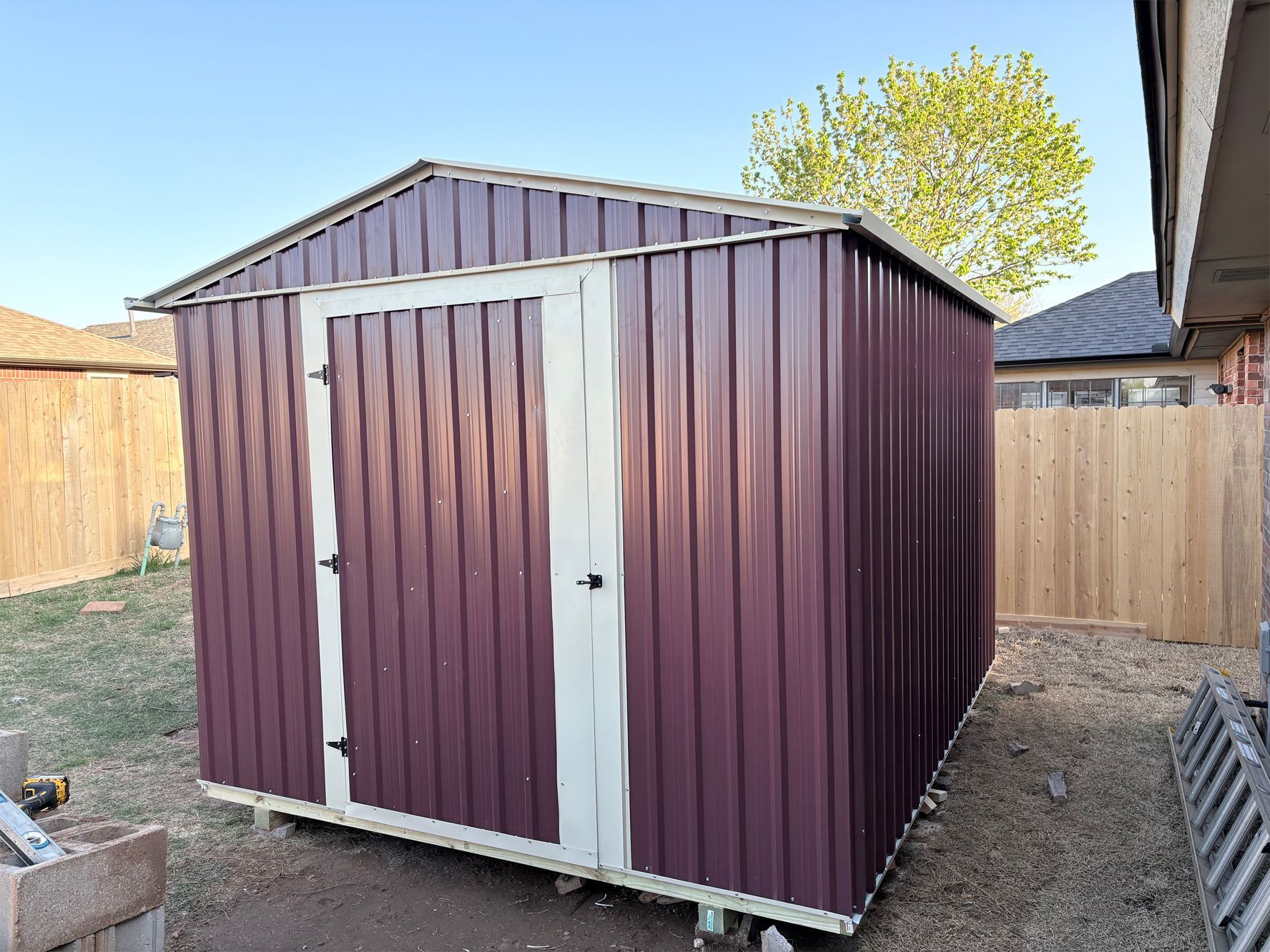A purple metal shed is sitting in a backyard next to a wooden fence.