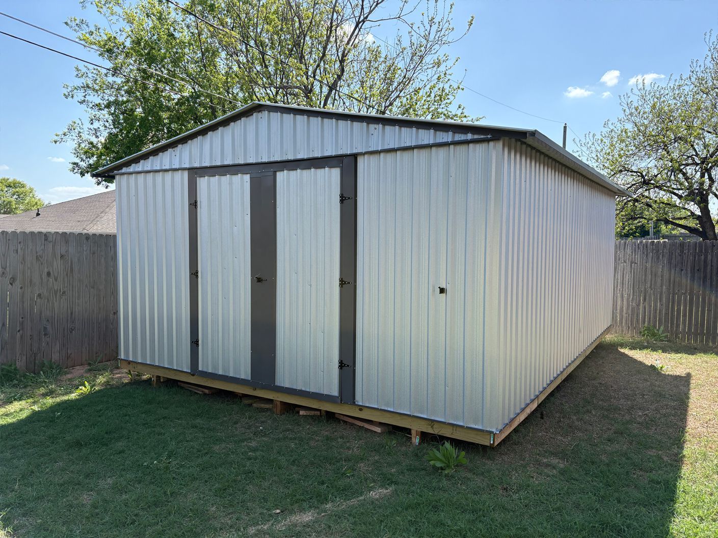 A metal shed is sitting on top of a wooden platform in a backyard.