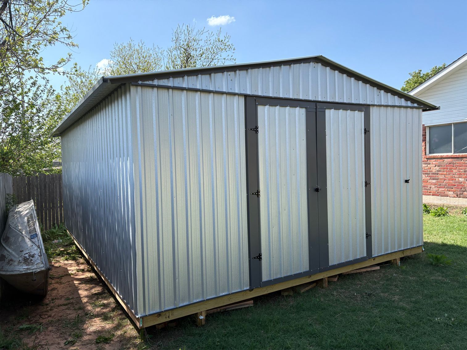 A metal shed is sitting in the grass in front of a house.