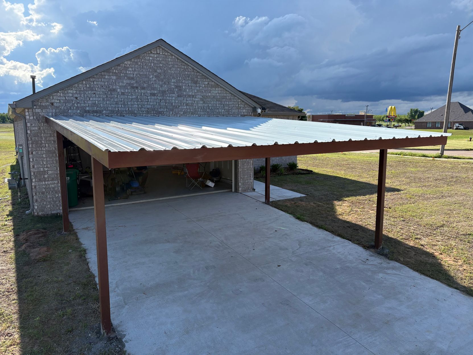 A carport with a metal roof is attached to a brick building.