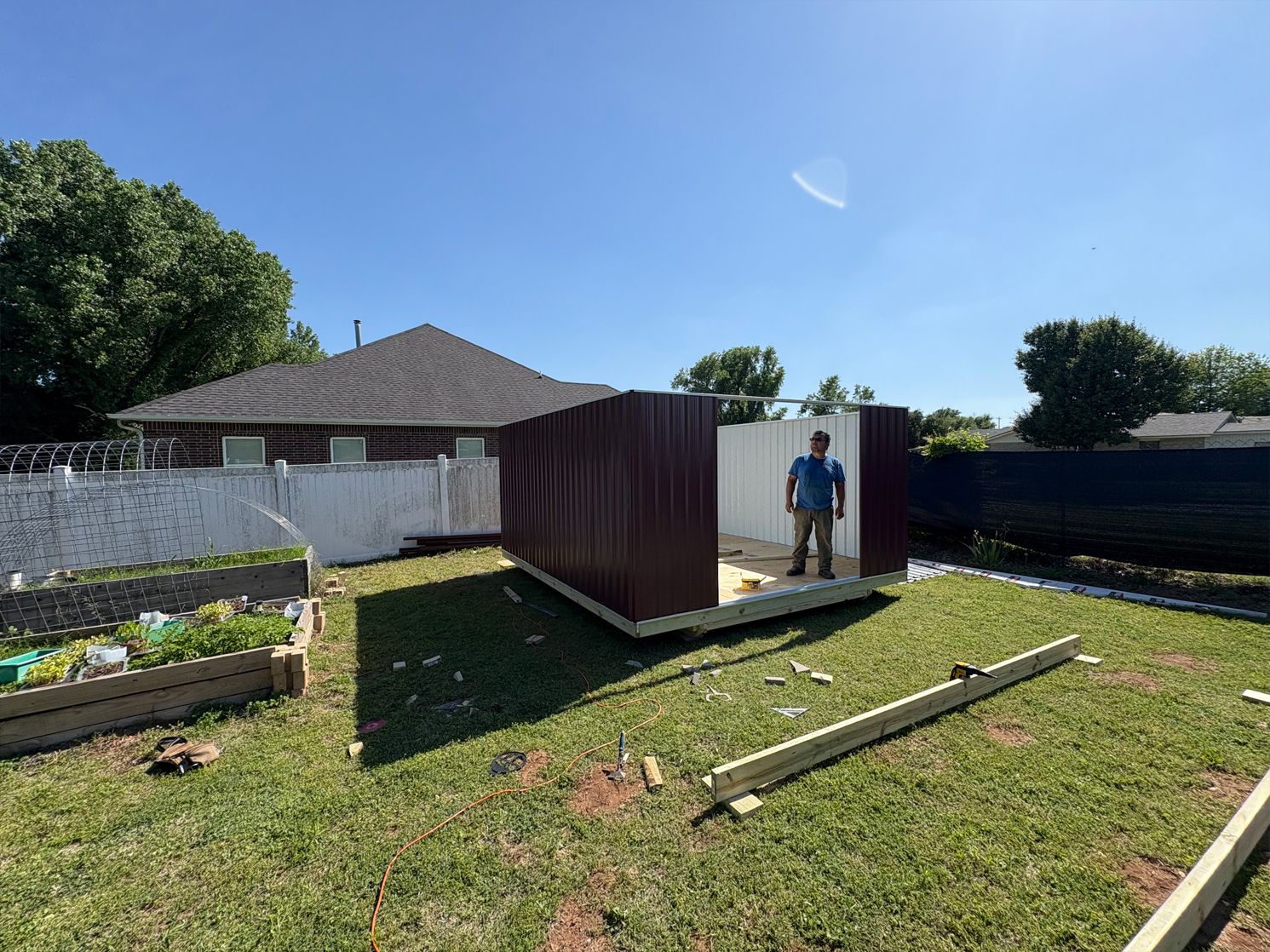 A man is standing in front of a shed in a backyard.