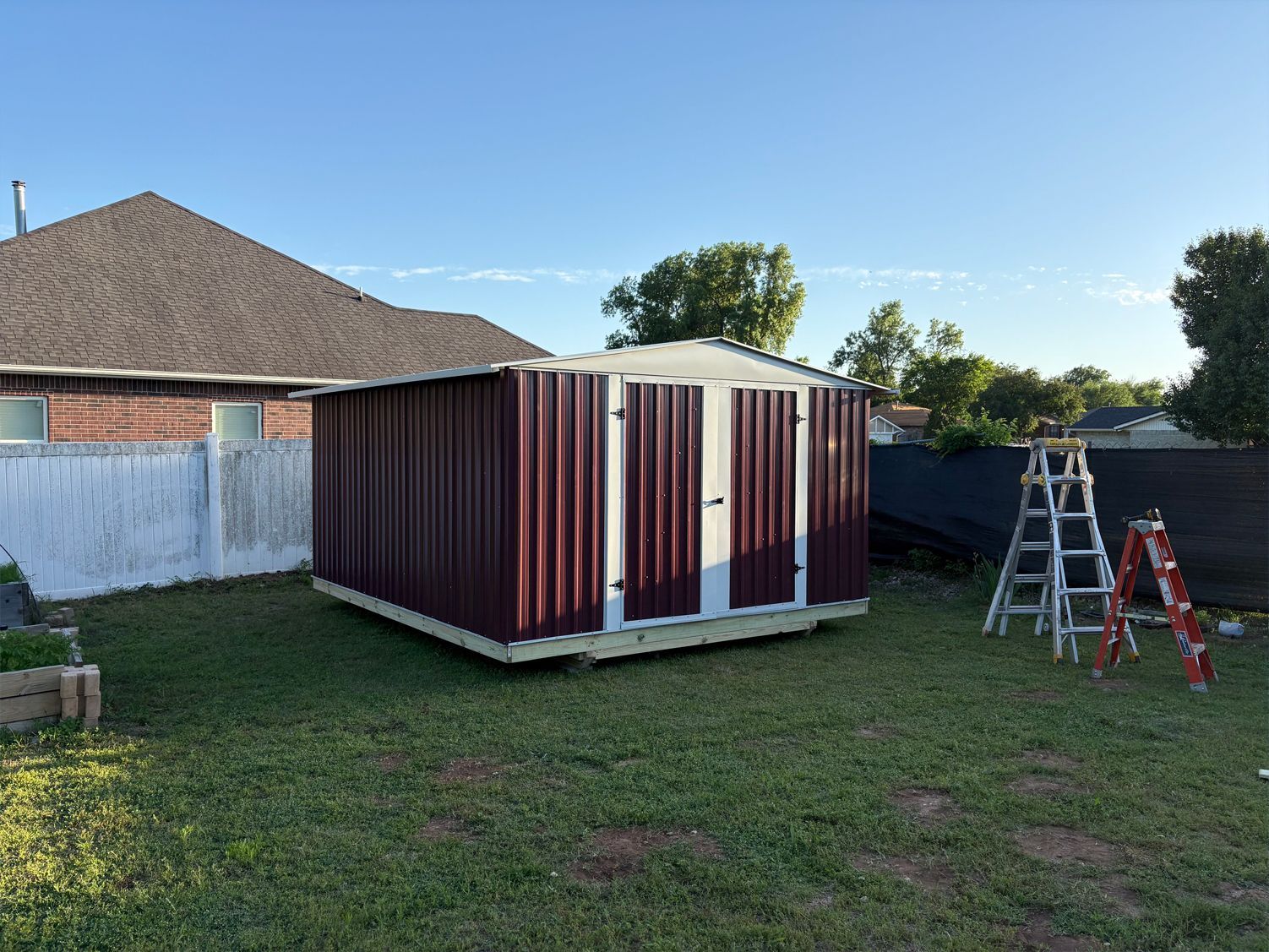 A shed is sitting in the grass in front of a house.