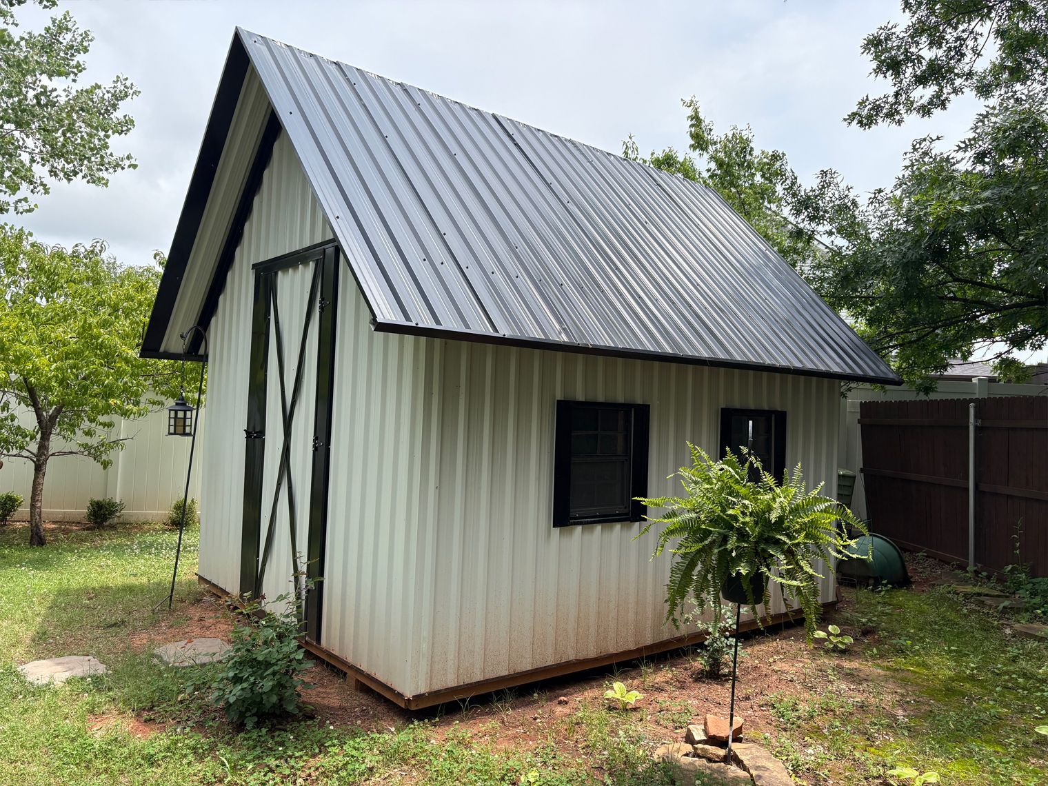 A white shed with a black roof is sitting in the middle of a yard.