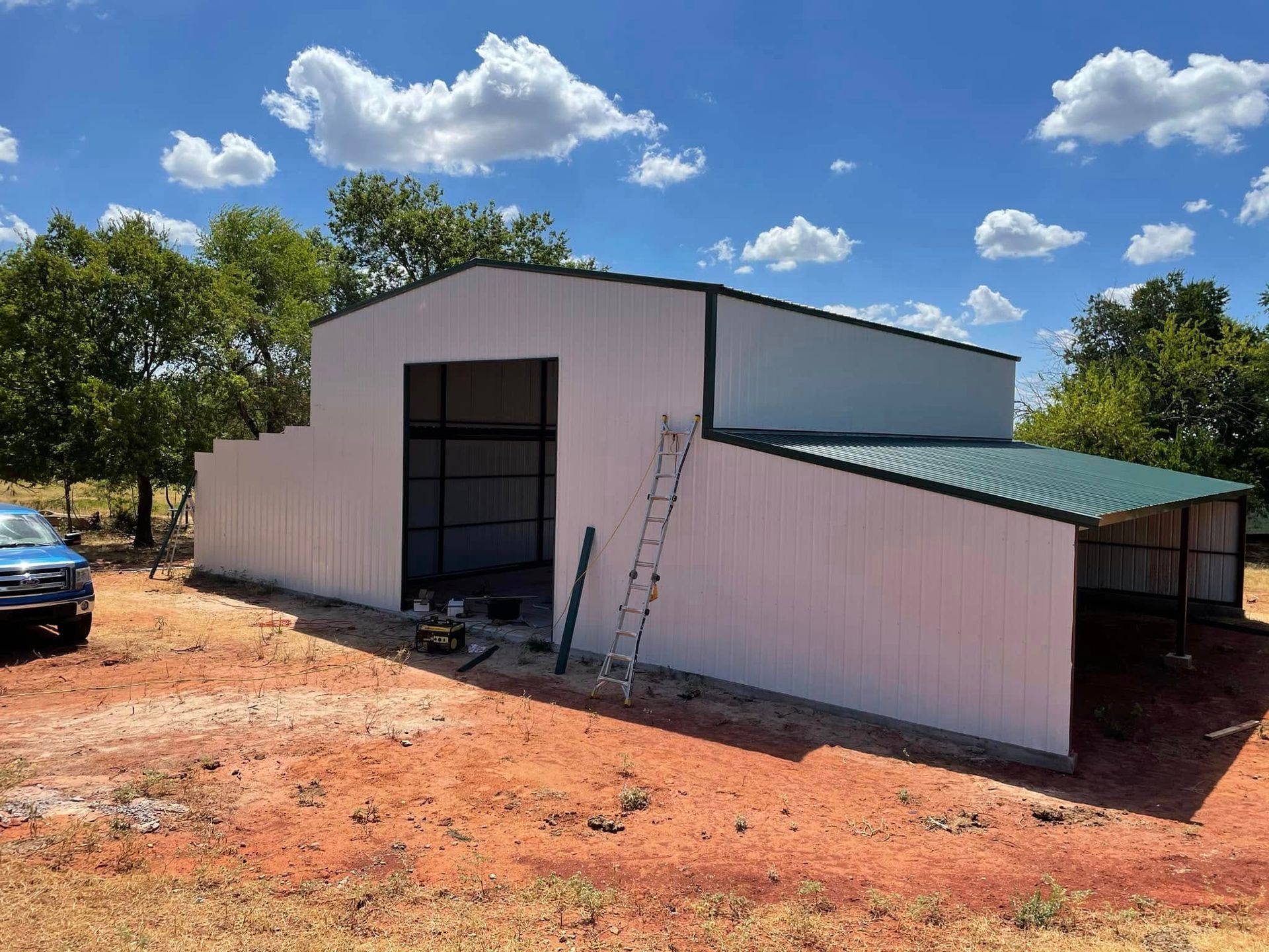 A white metal building with a green roof and a blue truck parked in front of it.