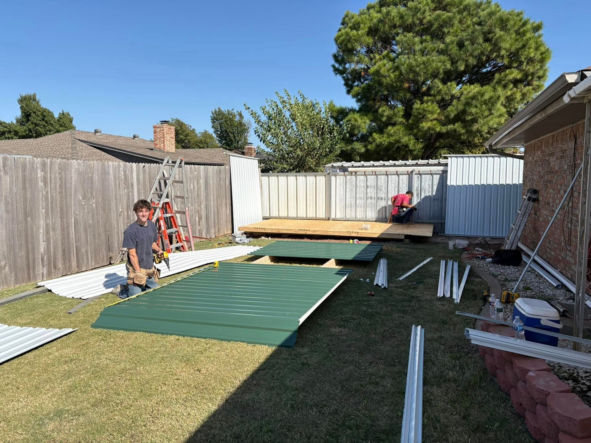 A man is kneeling on the grass in front of a fence in a backyard.