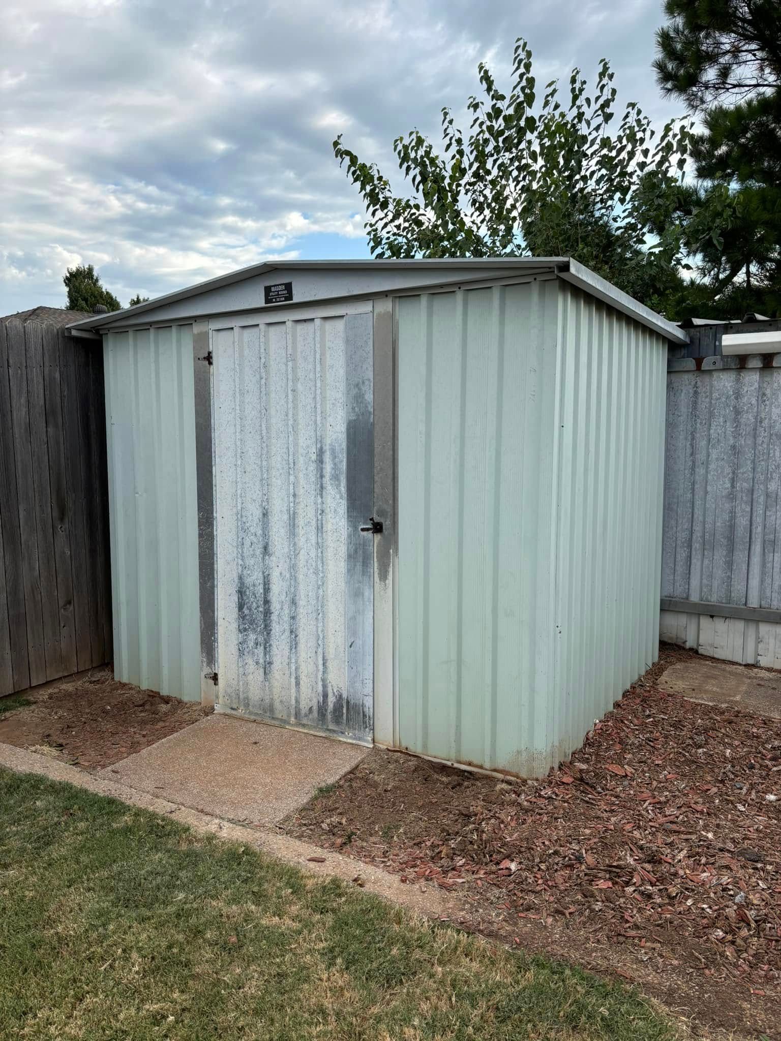 A white metal shed is sitting in the backyard next to a wooden fence.
