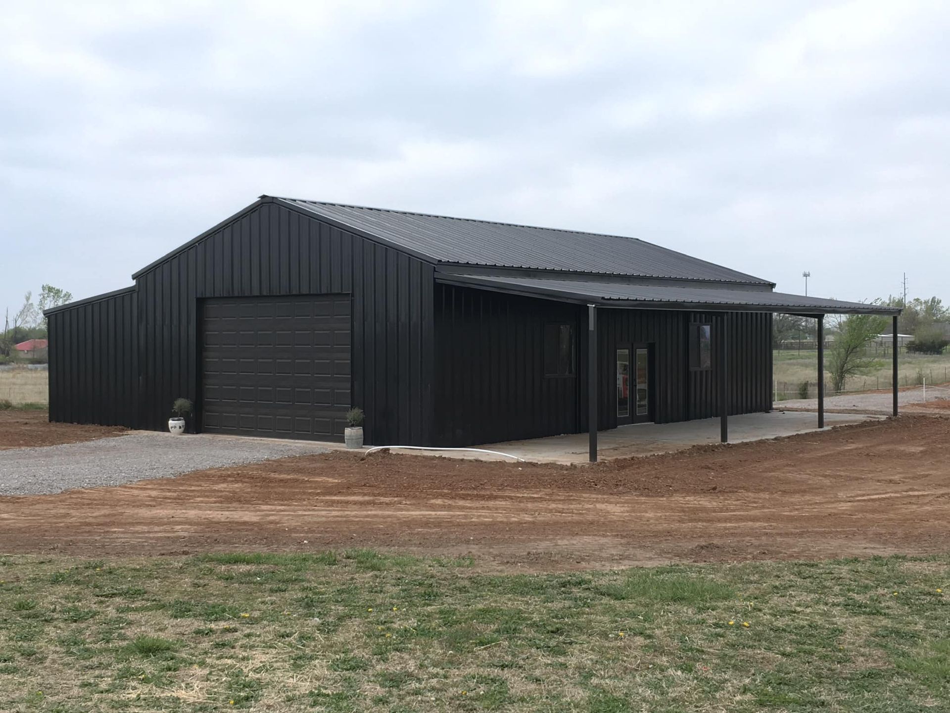 A black metal building with a porch is sitting in the middle of a field.