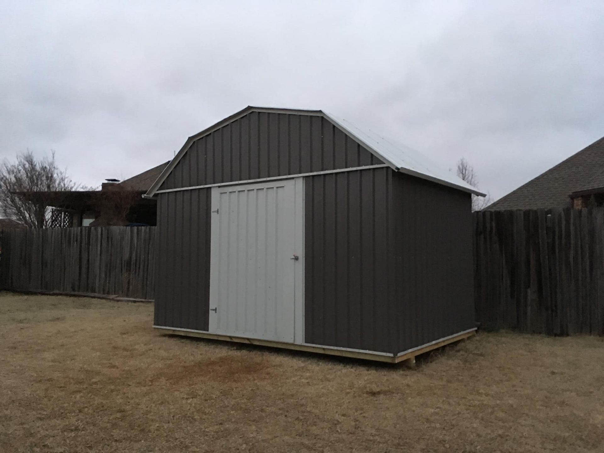 A shed with a white door is in a backyard next to a wooden fence.