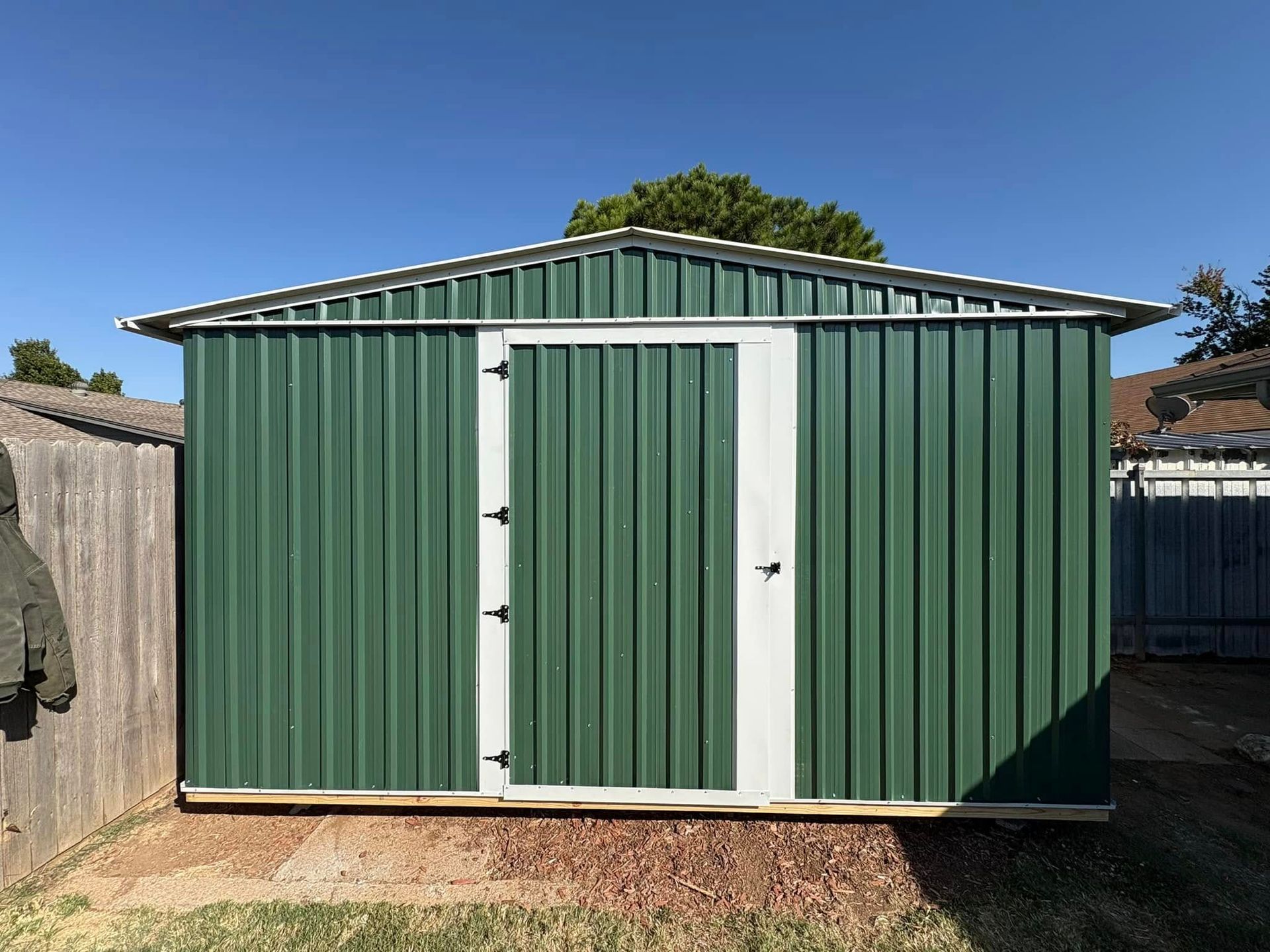 A green metal shed with a white door in a backyard.