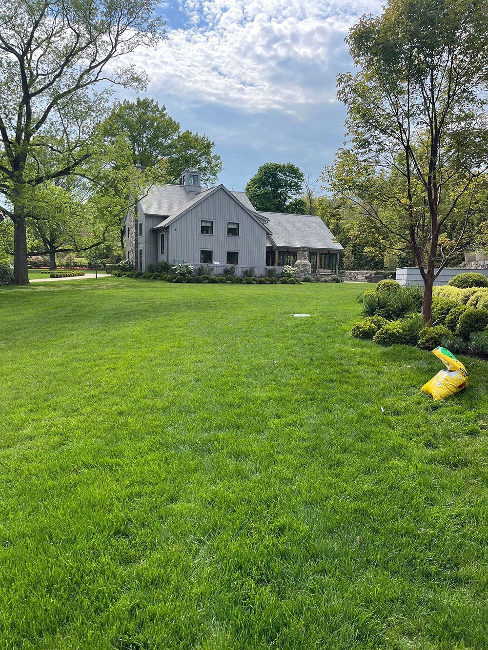 Gray house with screened porch in a green yard under a partly cloudy sky, with a yellow bag on the grass
