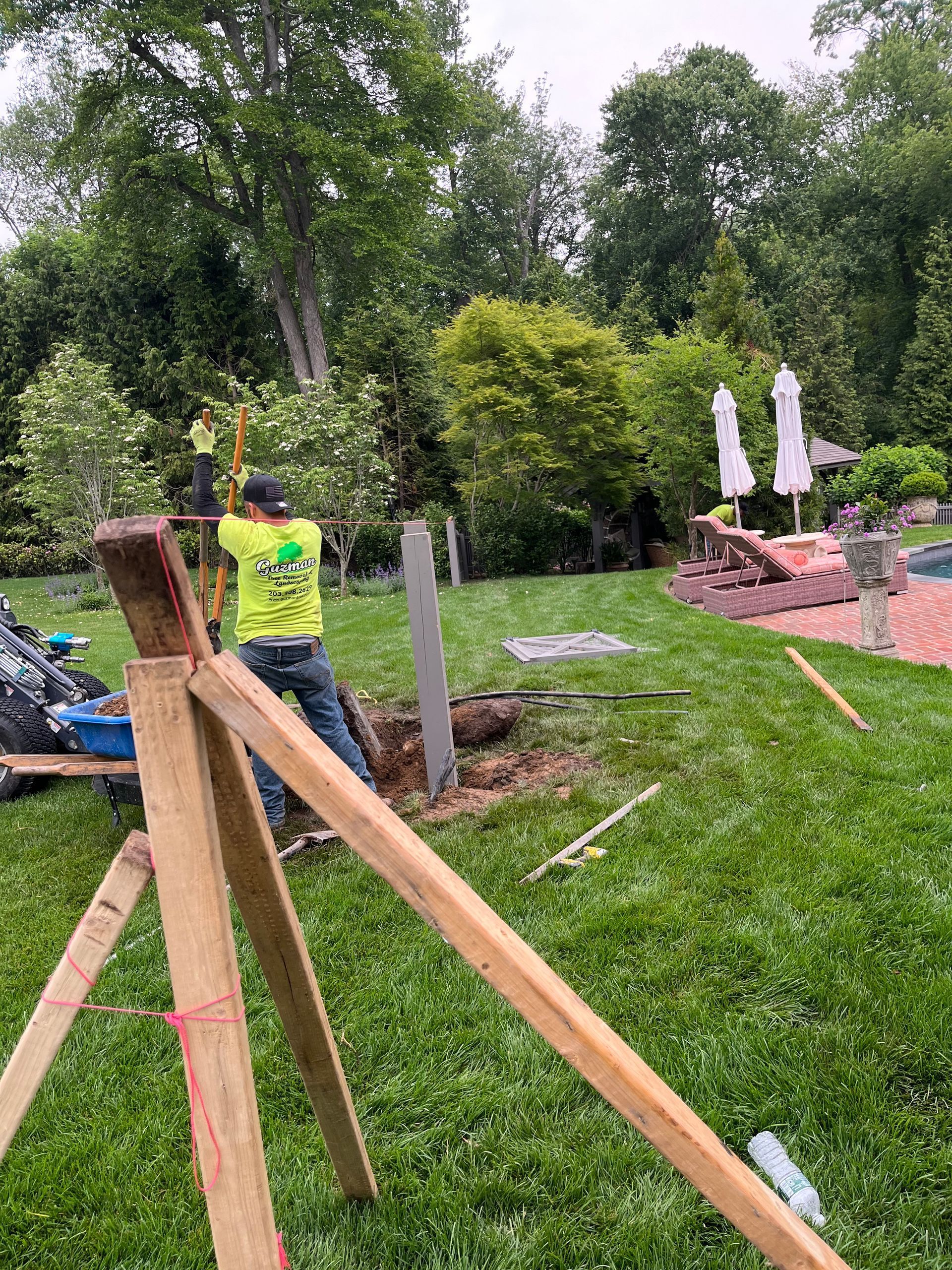 Outdoor construction scene with wooden posts, a worker in a neon vest, and stacked stone in a grassy yard