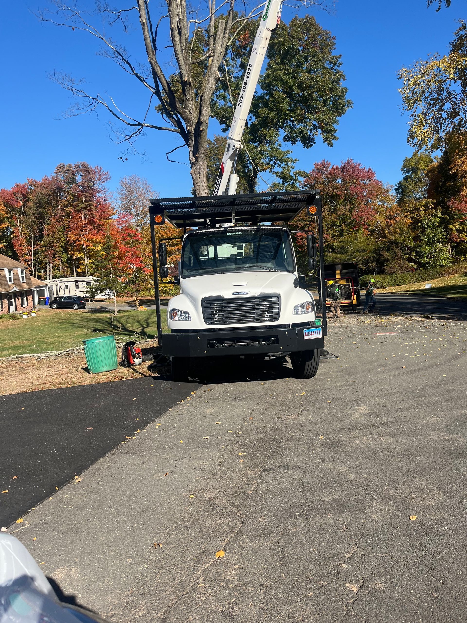 White utility truck parked on a paved driveway under autumn trees
