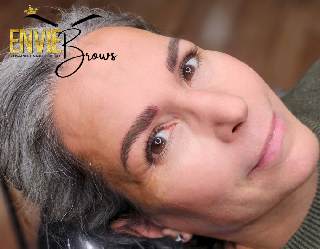 A woman with gray hair and brown eyebrows is laying down and smiling.