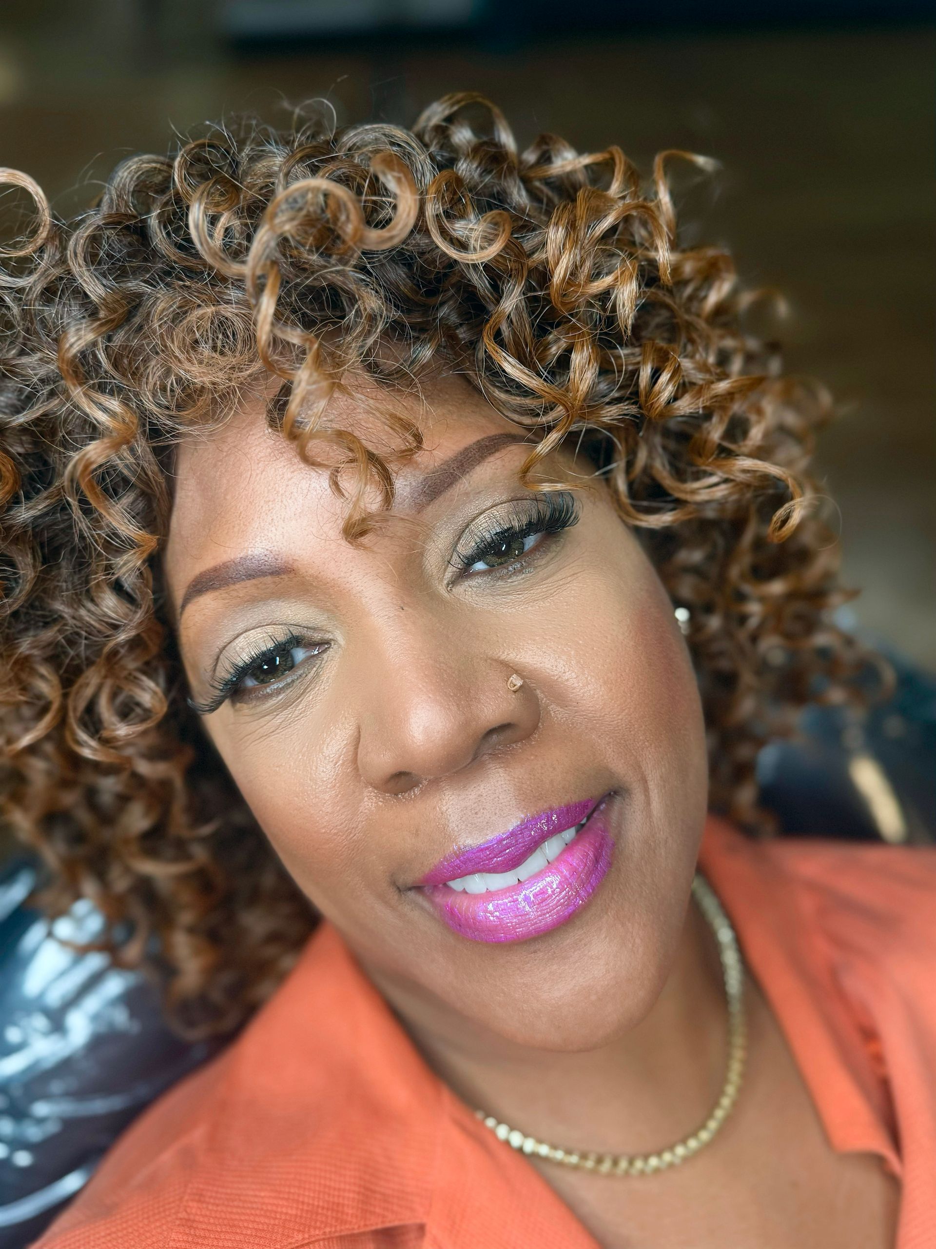 A woman with curly hair and pink lipstick is smiling for the camera.