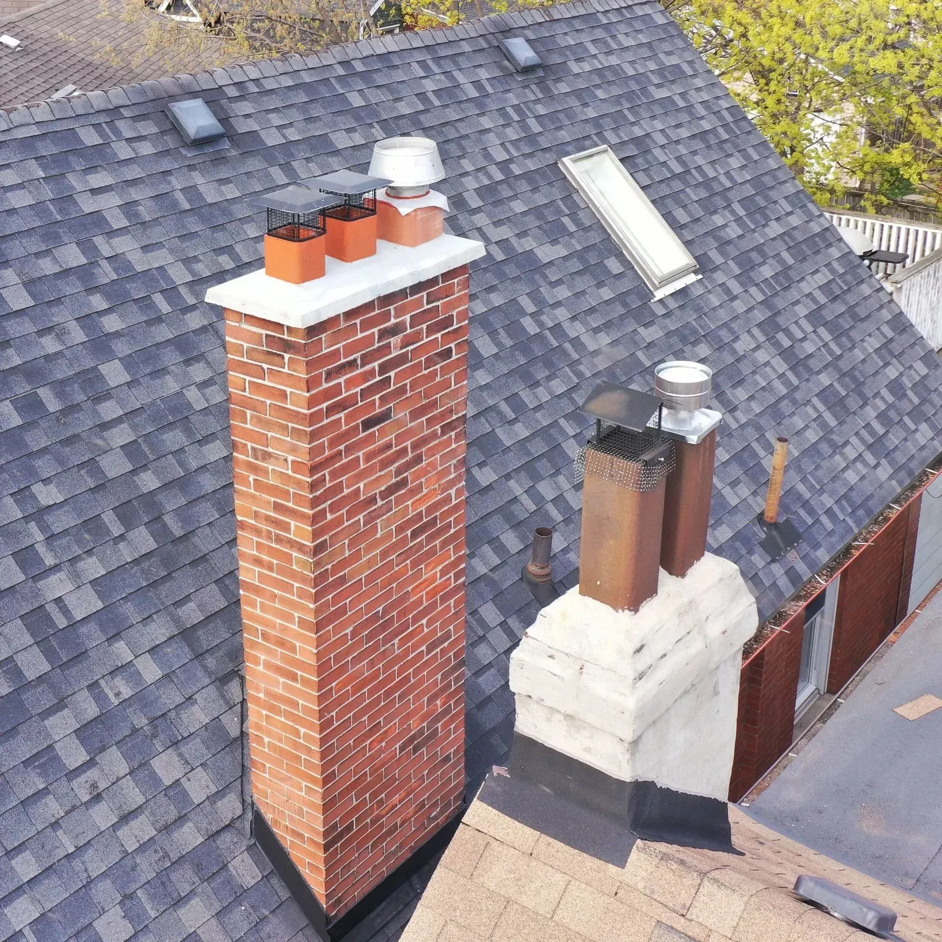 Aerial view of two brick chimneys on a gray shingled roof with rooftop vents and skylights.