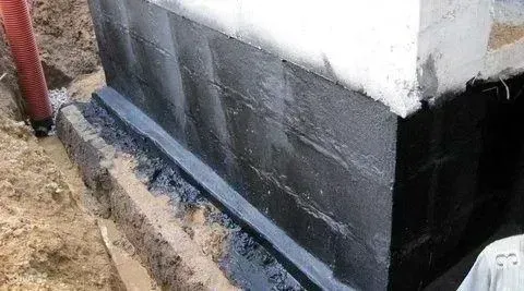 Black waterproofing coating applied to the lower exterior wall of a building near the ground