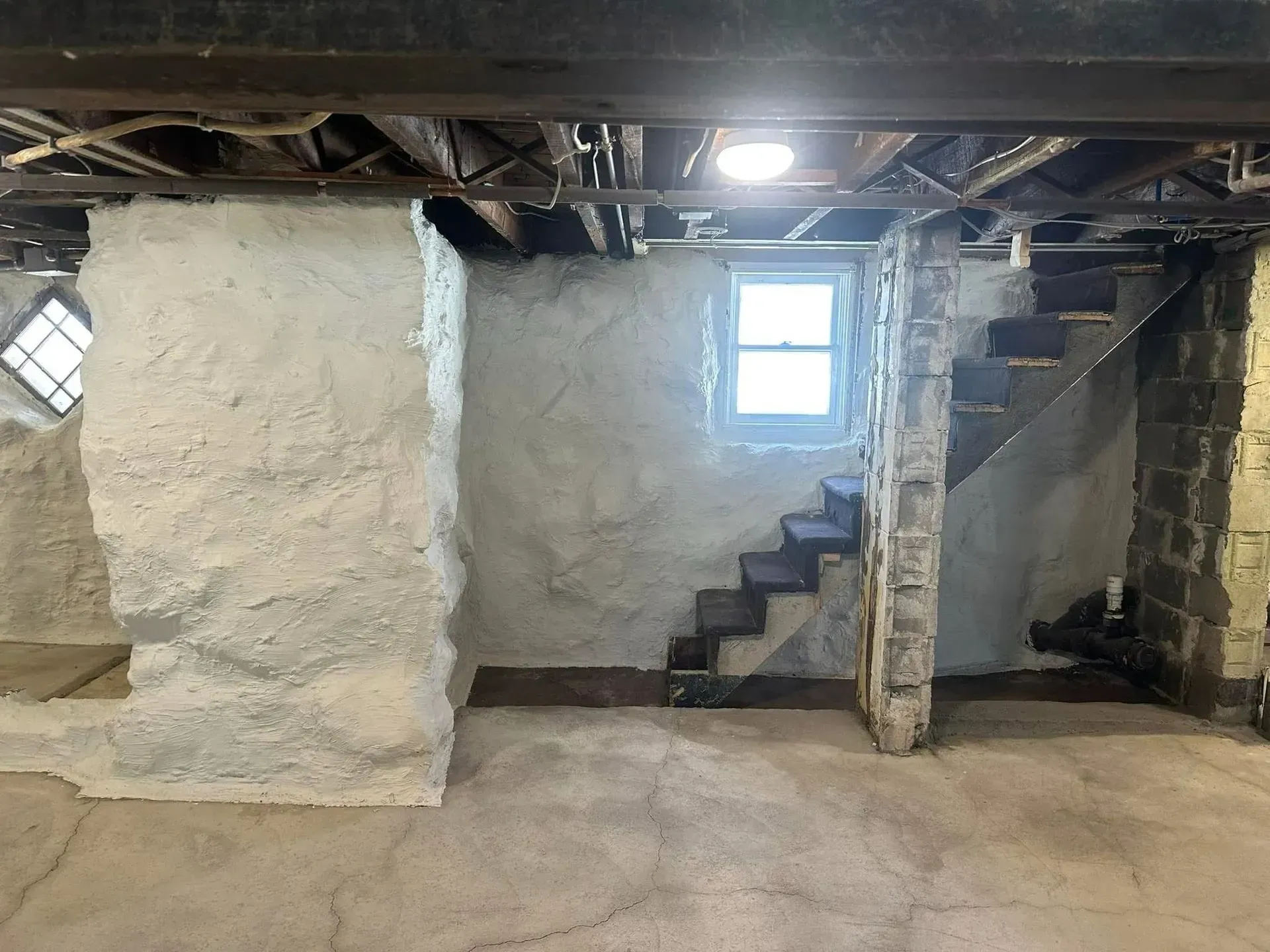 Basement interior with rough stone walls, exposed beams, small window, and stairs leading up to a door.