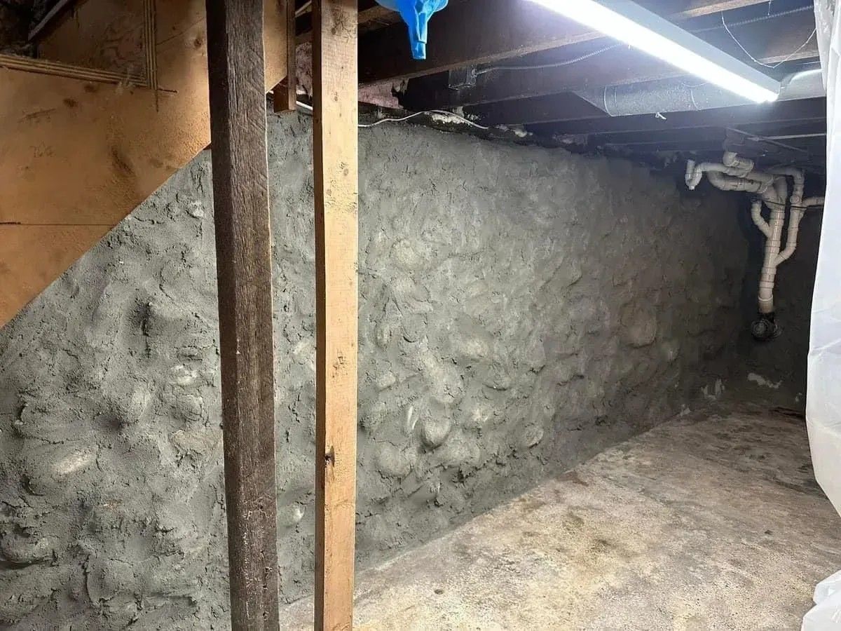 Small rough-plastered basement room with exposed ceiling beams and a fluorescent light.