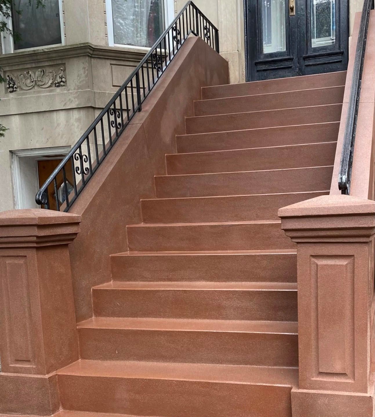 Brown stone staircase leading to a building entrance with black iron railings and brownstone facade.