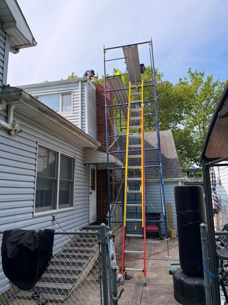 Tall yellow ladder beside a house, leading to a roof under construction in a backyard
