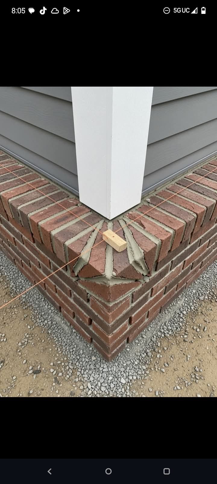 Corner of a house with brick foundation and white trim, showing a damaged piece at the base.