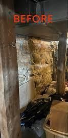 Before photo of a narrow, damaged interior space with exposed insulation, debris, and black plastic covering the floor