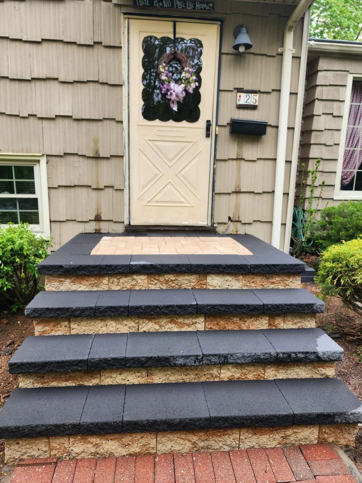 Front porch steps leading to a cream door with floral wreath and tan siding on a house