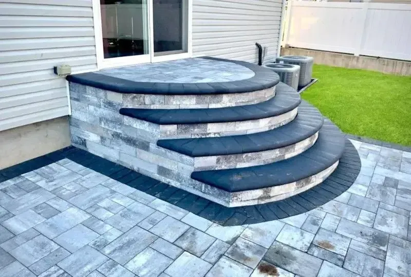 Curved stone patio steps with dark treads leading to a raised circular platform beside a house