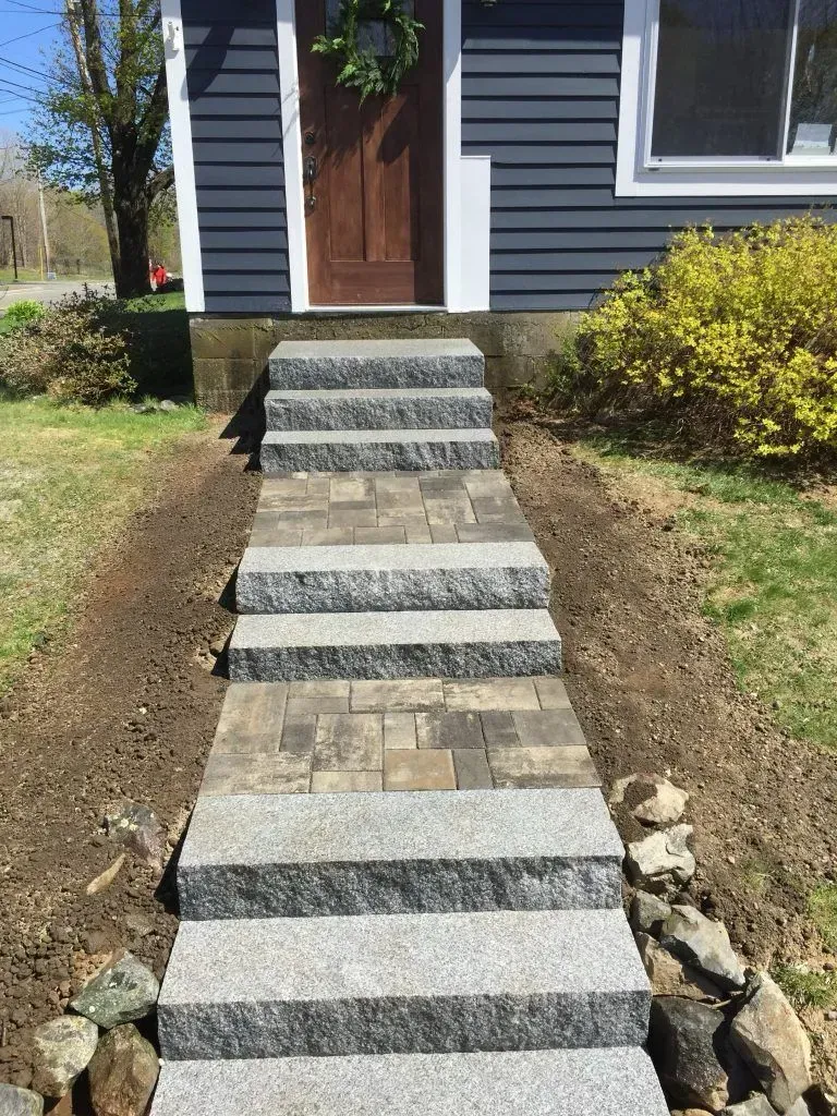 Stone walkway and steps leading to a dark blue house front door, bordered by grass and rocks.